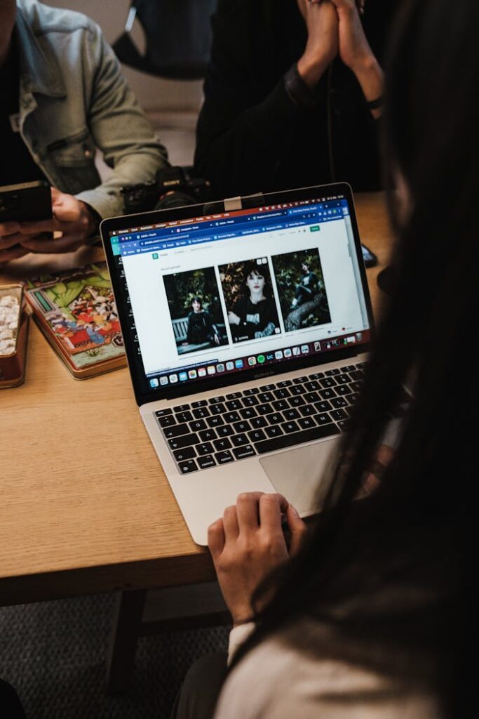 A woman browsing photos on a laptop during an informal meeting at a wooden table.